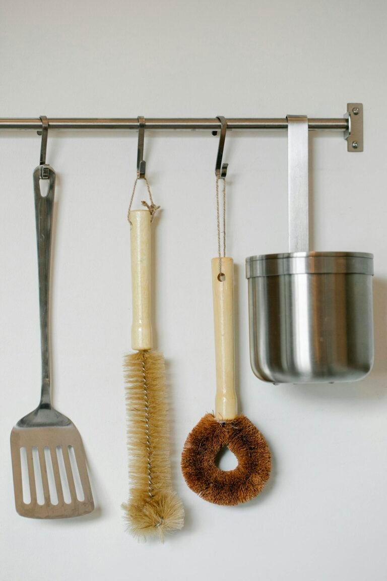 Diverse kitchen utensils including brush and stainless tools on wall hanger.