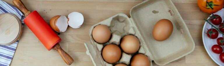 High angle view of eggshells, tomatoes, and rolling pin on a wooden surface.